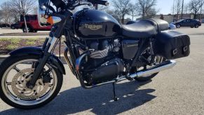 The side 3/4 view of a black 2009 Triumph Bonneville with saddlebags rented on Twisted Road in a parking lot