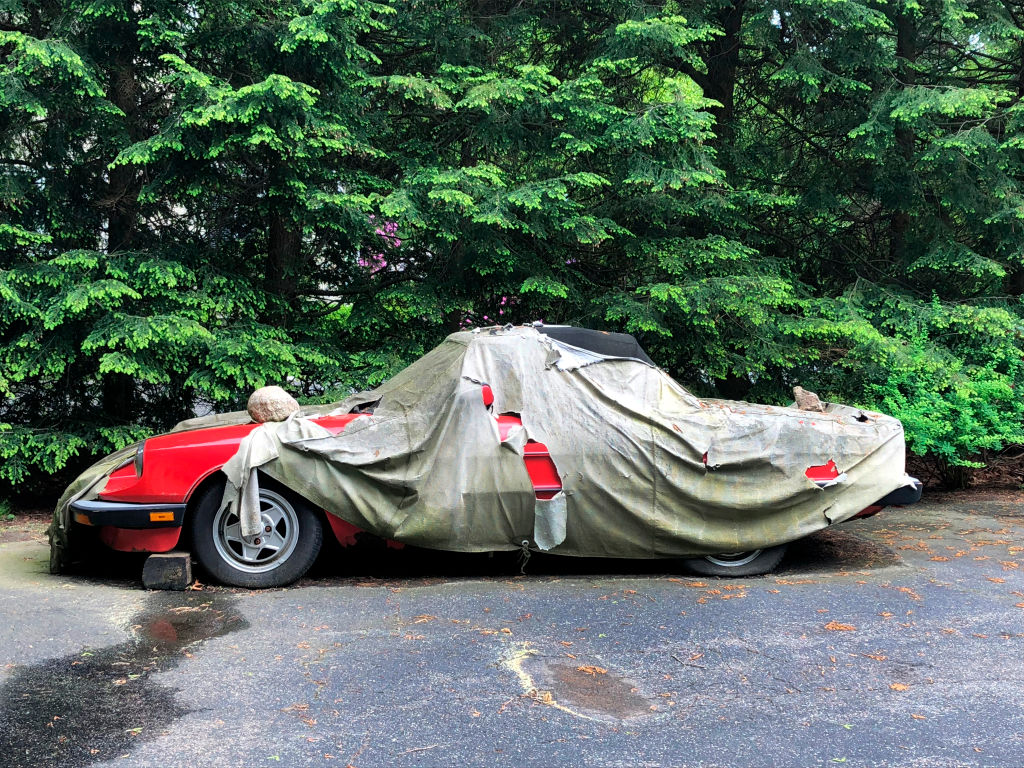 A rusted red classic Ferrari underneath an old ripped protective covering