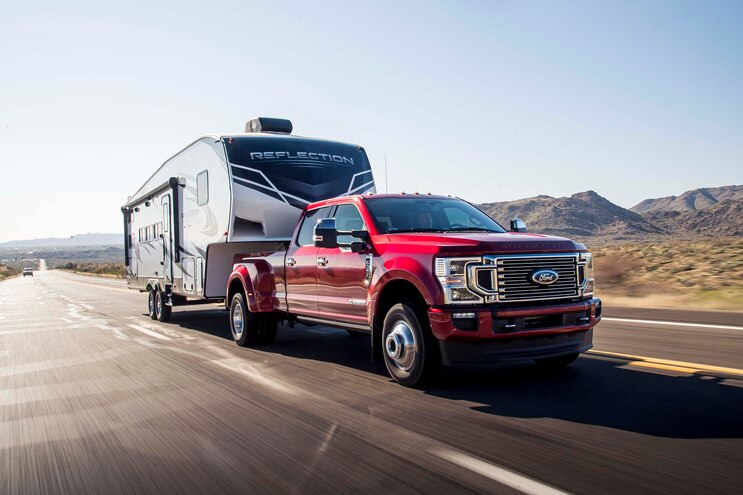 A red 2021 Ford F-350 Super Duty hauling a camper in a rural area