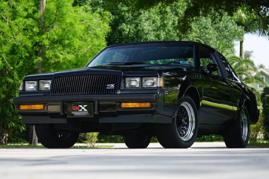 The front 3/4 view of a 262-mile black 1987 Buick GNX in a tree-lined parking lot