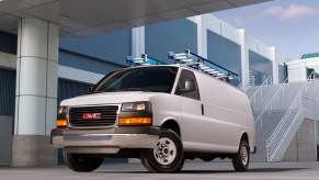 A white 2014 GMC Savana cargo van parked next to a modern white building