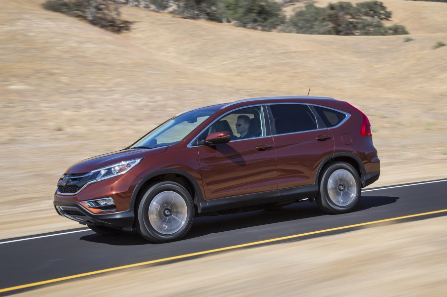 A dark-red metalllic 2016 Honda CR-V compact SUV travelinig on a road past hills with dry brown grass