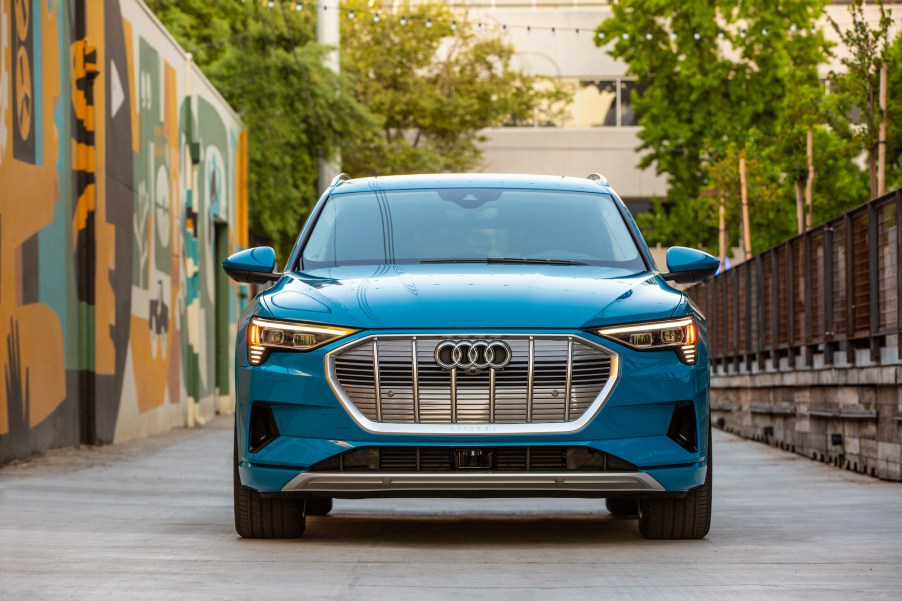 Front view of a turquoise-blue 2019 Audi e-tron electric SUV parked next to an abstract mural in a city