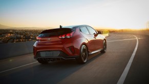 An orange 2019 Hyundai Veloster Turbo hatchback traveling on a road above a city