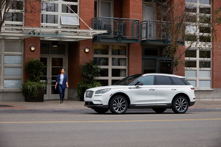 A white 2020 Lincoln Corsair is parked on a city street as a woman in blue exits a red-brick building