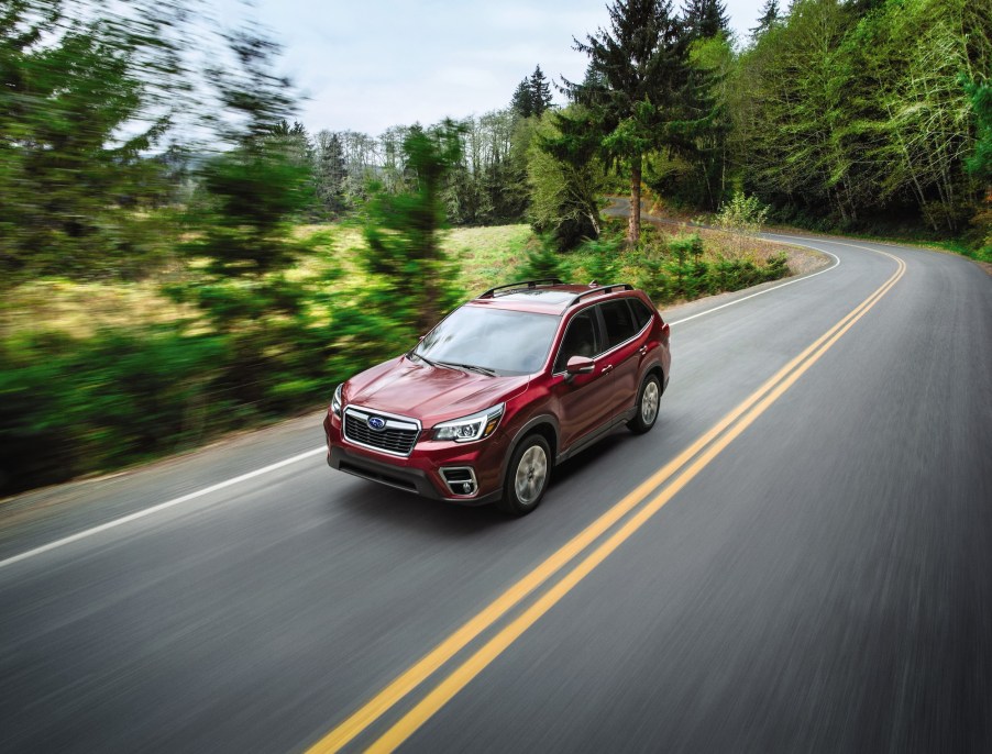 A dark-red 2020 Subaru Forester traveling on a two-lane highway through lush trees