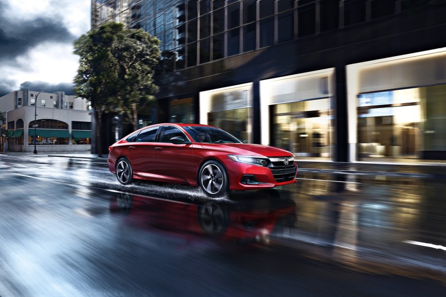 A red 2021 Accord Sport 2.0T midsize sedan travels on a wet city street on a cloudy day