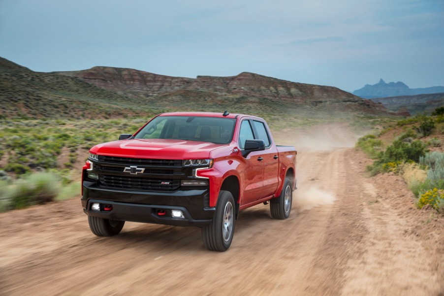 A red 2021 Chevrolet Silverado LT Trail Boss travels on a dirt road past mountains