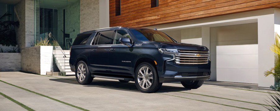 a blue 2021 Chevrolet suburban parked in front a modern garage with wood detail on the structure above