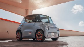 A gray 2021 Citroen Ami plugged into an outlet in a sunny parking garage