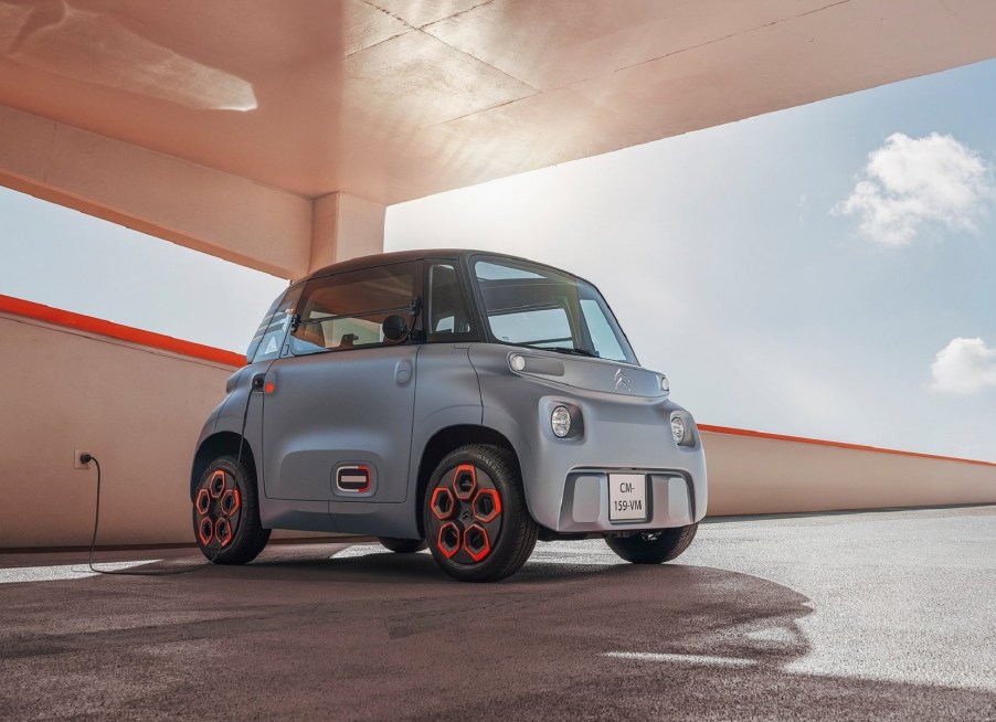 A gray 2021 Citroen Ami plugged into an outlet in a sunny parking garage