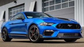 A blue 2021 Ford Mustang Mach 1 parked by a racetrack garage