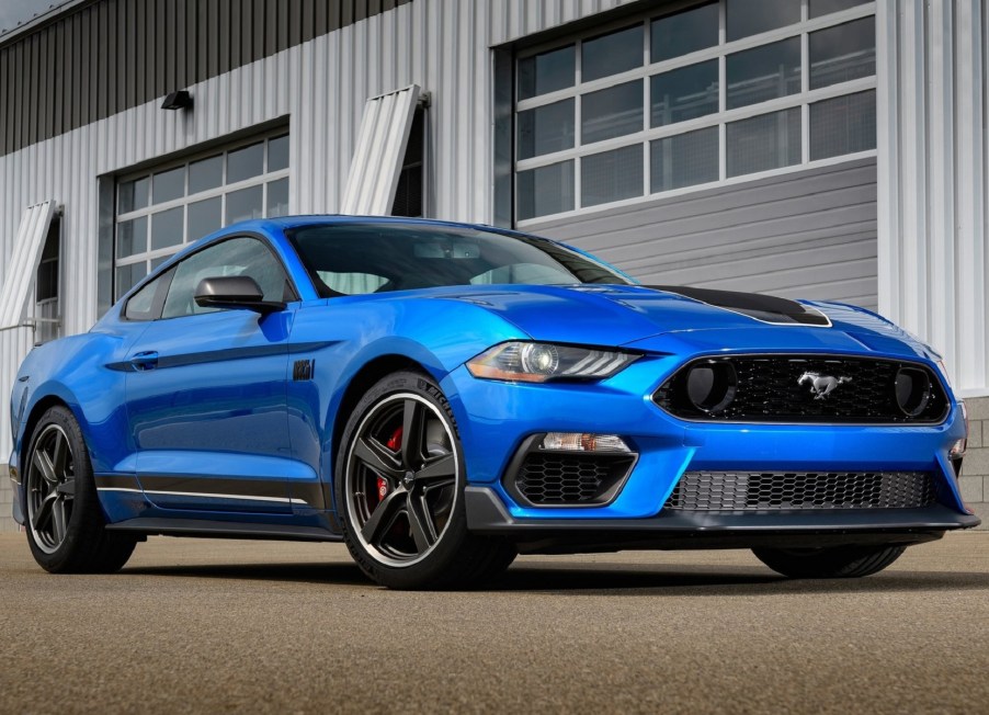 A blue 2021 Ford Mustang Mach 1 parked by a racetrack garage