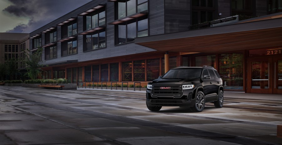 A black 2021 GMC Acadia Elevation midsize SUV parked in front of a brown modern building