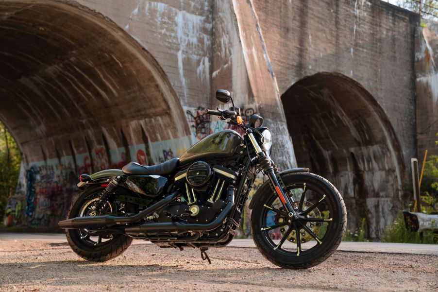 An olive-green 2021 Harley-Davidson Iron 883 Sportster next to a concrete bridge