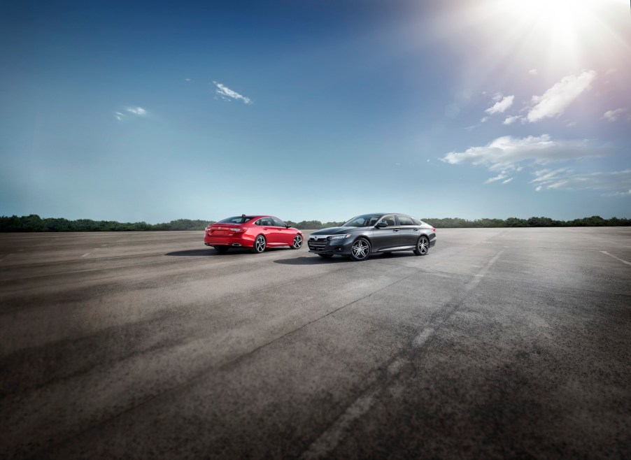 A red 2021 Honda Accord Sport SE and a dark-gray metallic Accord Hybrid parked on a large slab of asphalt on a sunny day