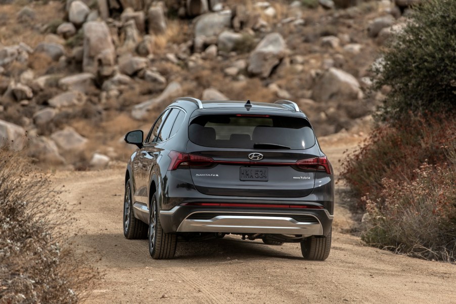 A rear view of a dark-gray 2021 Hyundai Santa Fe midsize SUV on a mountain road