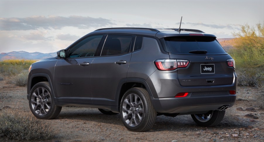 A dark-gray metallic 2021 Jeep Compass 80th Anniversary Edition compact crossover SUV parked on gravel in front of mountains in the distance