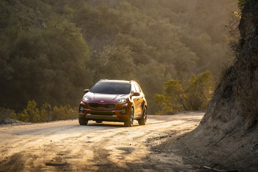 A red 2021 Kia Sportage compact SUV traveling on a dirt road between mountains