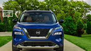 A blue 2021 Nissan Rogue parked in a suburban driveway with a basketball hoop