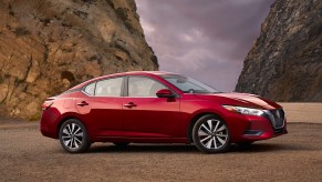 A red 2021 Nissan Sentra compact sedan parked between two mountains in front of dark clouds