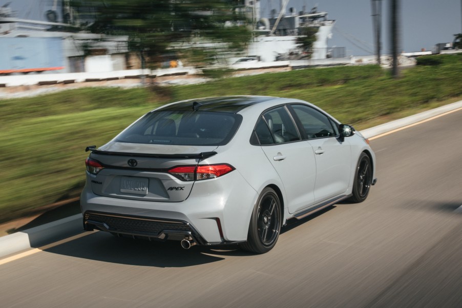 A light-gray 2021 Toyota Corolla Apex compact car travels on a road alongside a ship