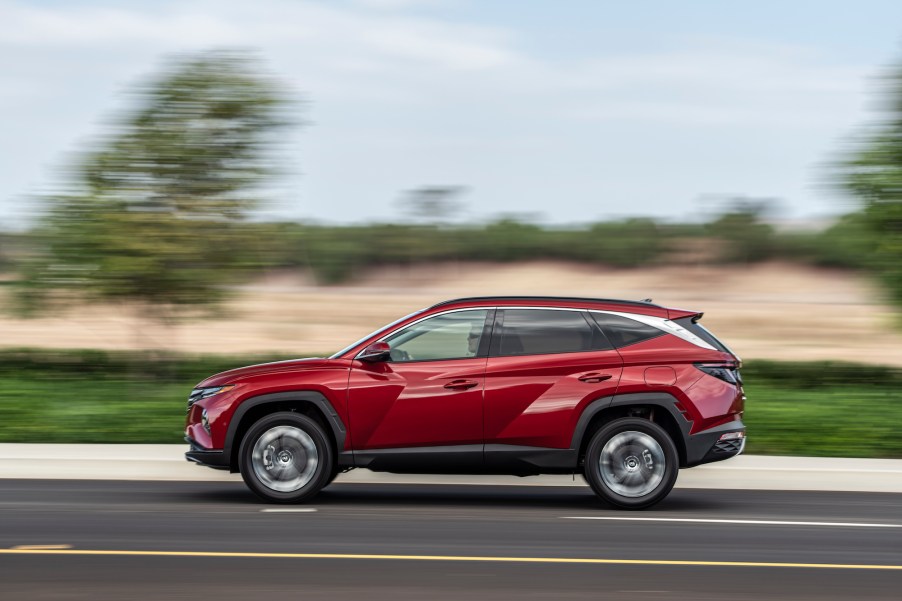 A red 2022 Hyundai Tucson travels on a highway along grass and trees. Hyundai and Kia are known for their generous car warranty coverage.