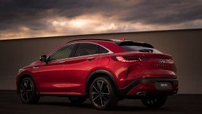 A red 2022 Infiniti QX55 AWD luxury compact crossover SUV parked next to a wall as dark clouds loom