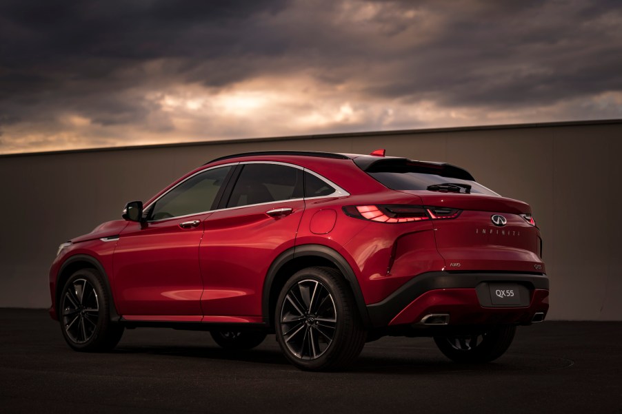 A red 2022 Infiniti QX55 AWD luxury compact crossover SUV parked next to a wall as dark clouds loom