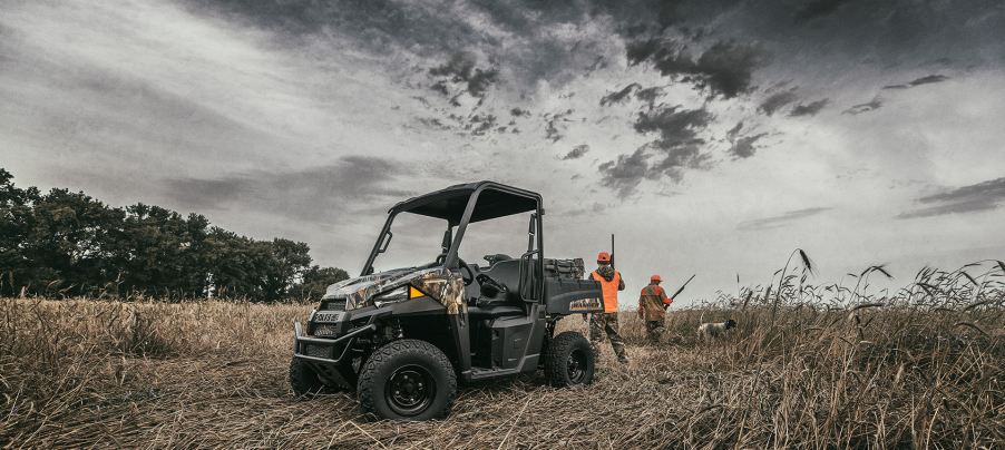 People in orange vests hunting in a field with a dog and the Polaris Ranger EV