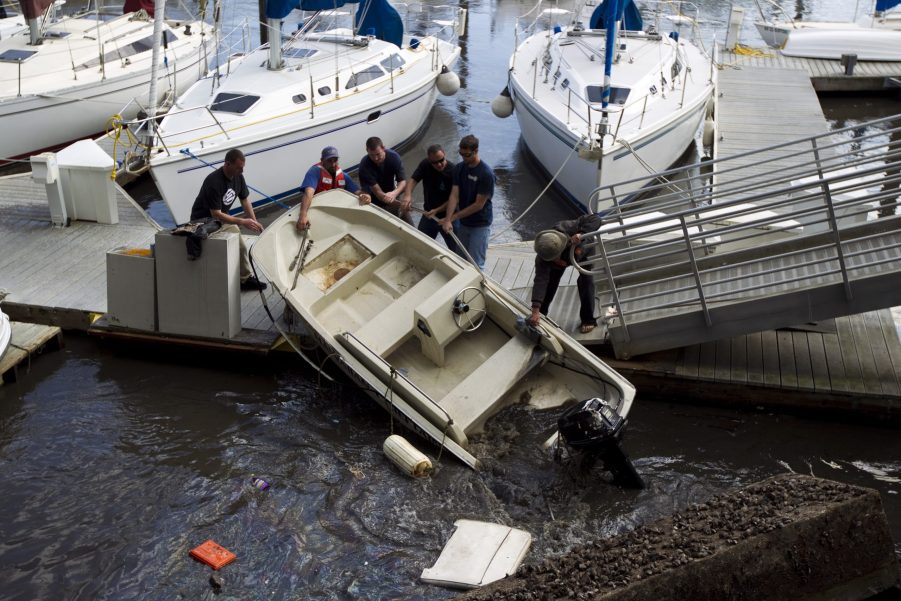 A group of people pull a Boston Whaler boat out of the water after it tipped over from a tsunami surge