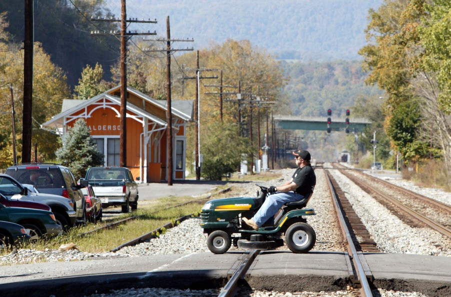 A man driving a lawnmower in the street, in many areas lawnmower driving laws say mowers aren't street legal