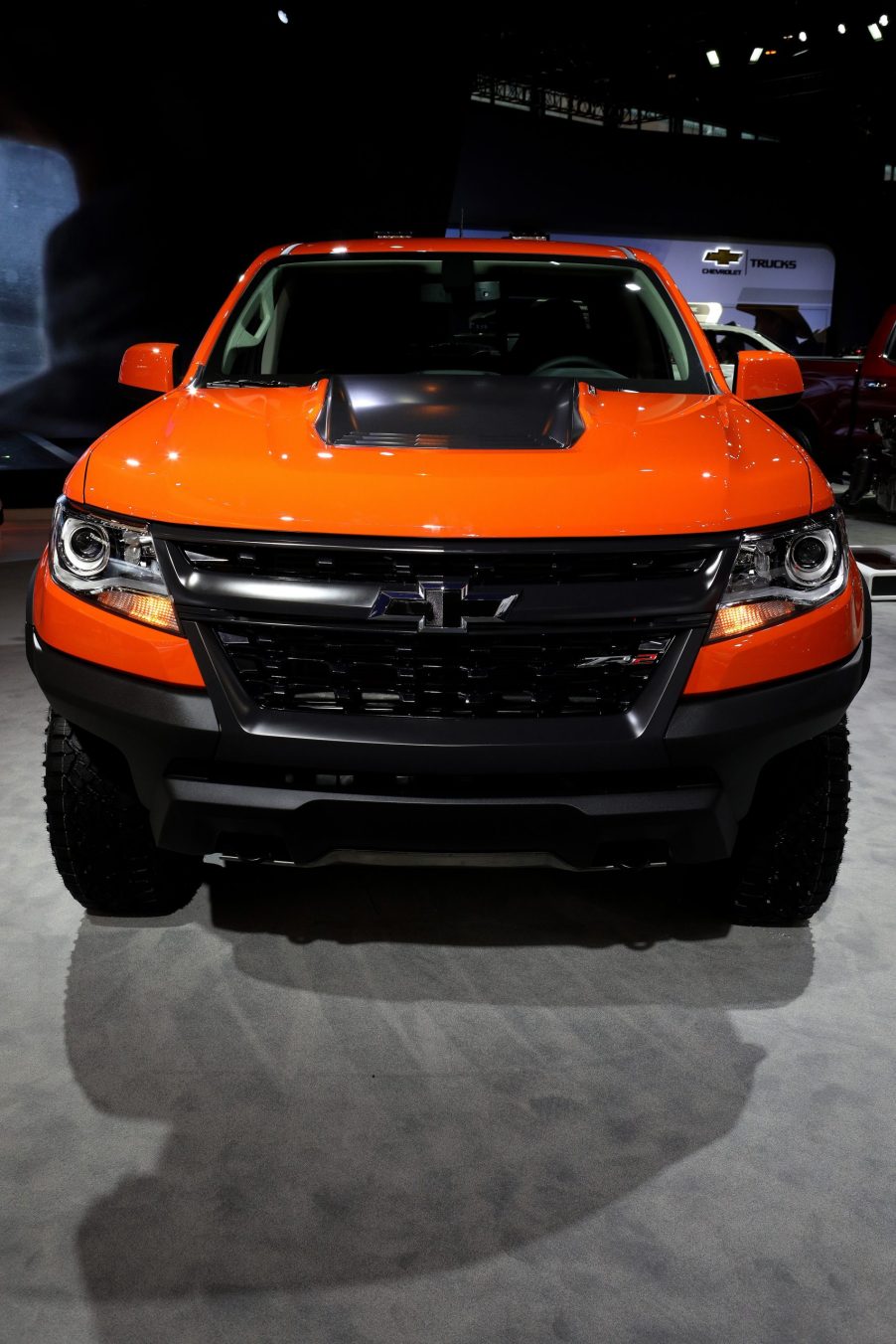 the front grille view of a bright orange Chevrolet Colorado on display at an auto show.