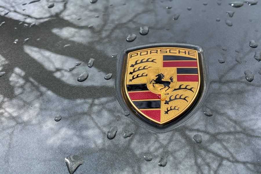 Porsche logo on a raindrop speckled car hood reflecting trees in the paint coat.