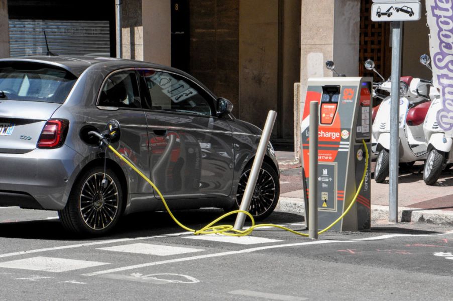 A silver Fiat 500 sits on a street plugged into an EV charger