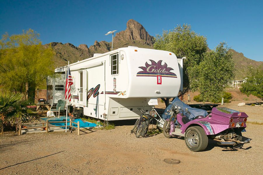 A camper RV traler unhitched at a campsite with bicycles and an off-road vehicle nearby.