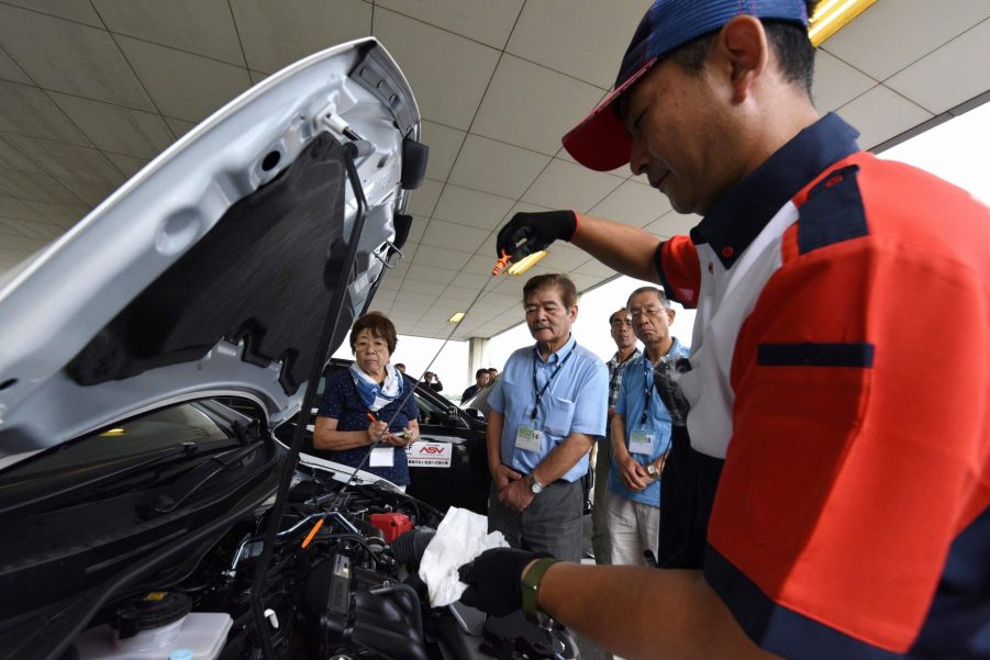 an instructor using a dipstick to check engine oil levels during a lesson on car maintenance at a driving school for senior citizens