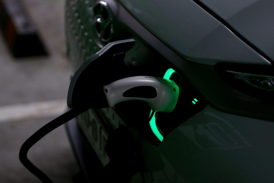 White Hyundai Kona EV SUV charging in a dark garage. The charging plug is lit in green.