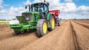 a green John Deere tractor with yellow wheels doing framework in a bare field