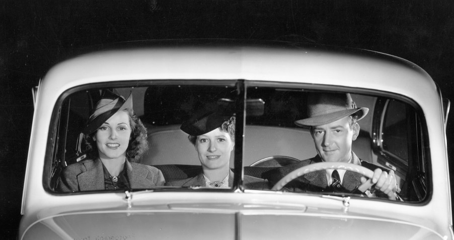 A black-and-white photo of a male driver and two female passengers in the front bench seat of a 1939 Oldsmobile