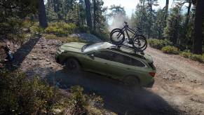 a green subaru outback with bikes on top climbing a forested hill