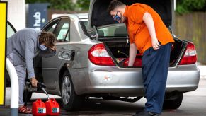 Two motorists fill up multiple gas cans and put them in their car