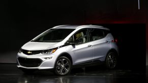 A silver Chevy Bolt under a lightbox at an auto show