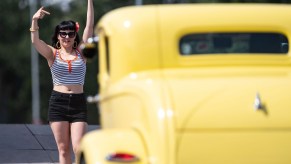 A woman waves at a yellow hot rod