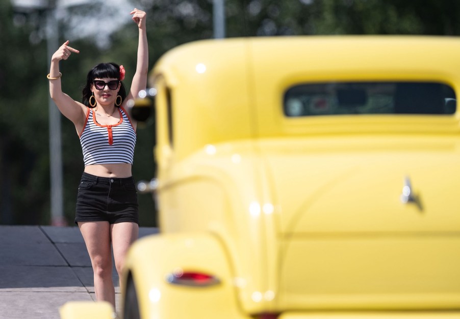 A woman waves at a yellow hot rod