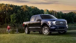 A navy blue Ford F150 in front of a lake while a man fishes and a woman carries a tackle box.