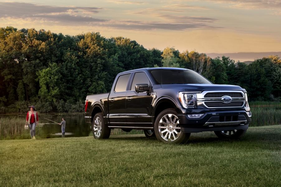 A navy blue Ford F150 in front of a lake while a man fishes and a woman carries a tackle box.