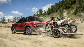 A dark-red 2021 Ford Bronco Sport SUV towing two dirt bikes on a dusty trail