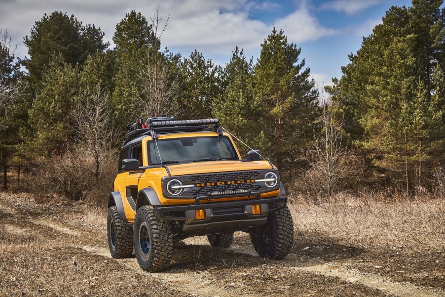 A yellow 2021 Ford Bronco compact SUV traveling on trail near a wooded area