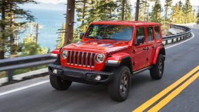 A red 2021 Jeep Wrangler Rubicon Unlimited drives on a forest road overlooking a lake